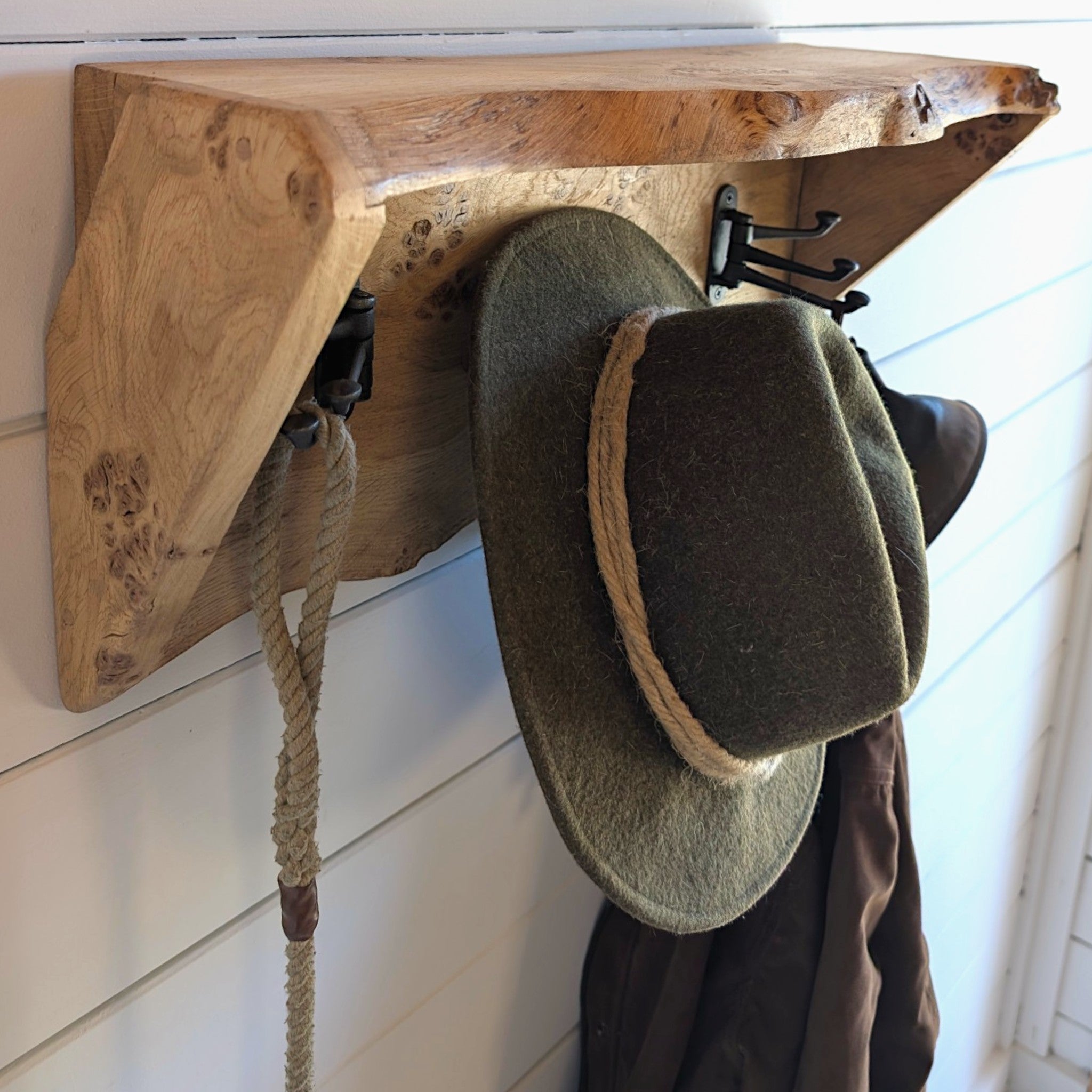 Thriverton live edge pippy oak coat rack and shelf with cast iron hooks holding a hat and rope on a white wall