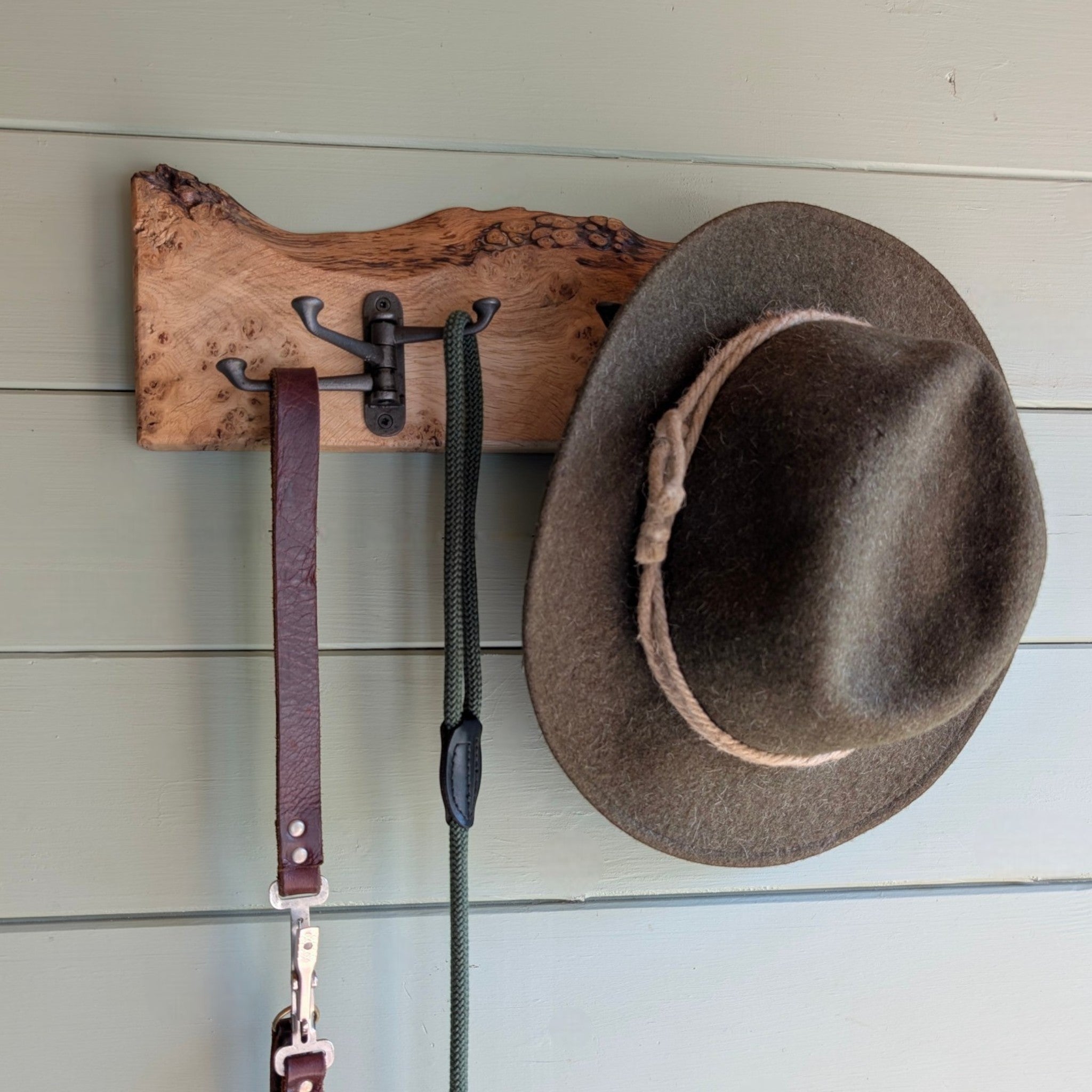 Thriverton live edge pippy oak coat rack with cast iron hooks holding a hat and leashes on a green wall